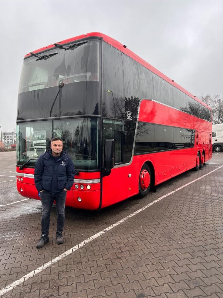 Obaidullah Karimi in front of a red Van Hool double-decker